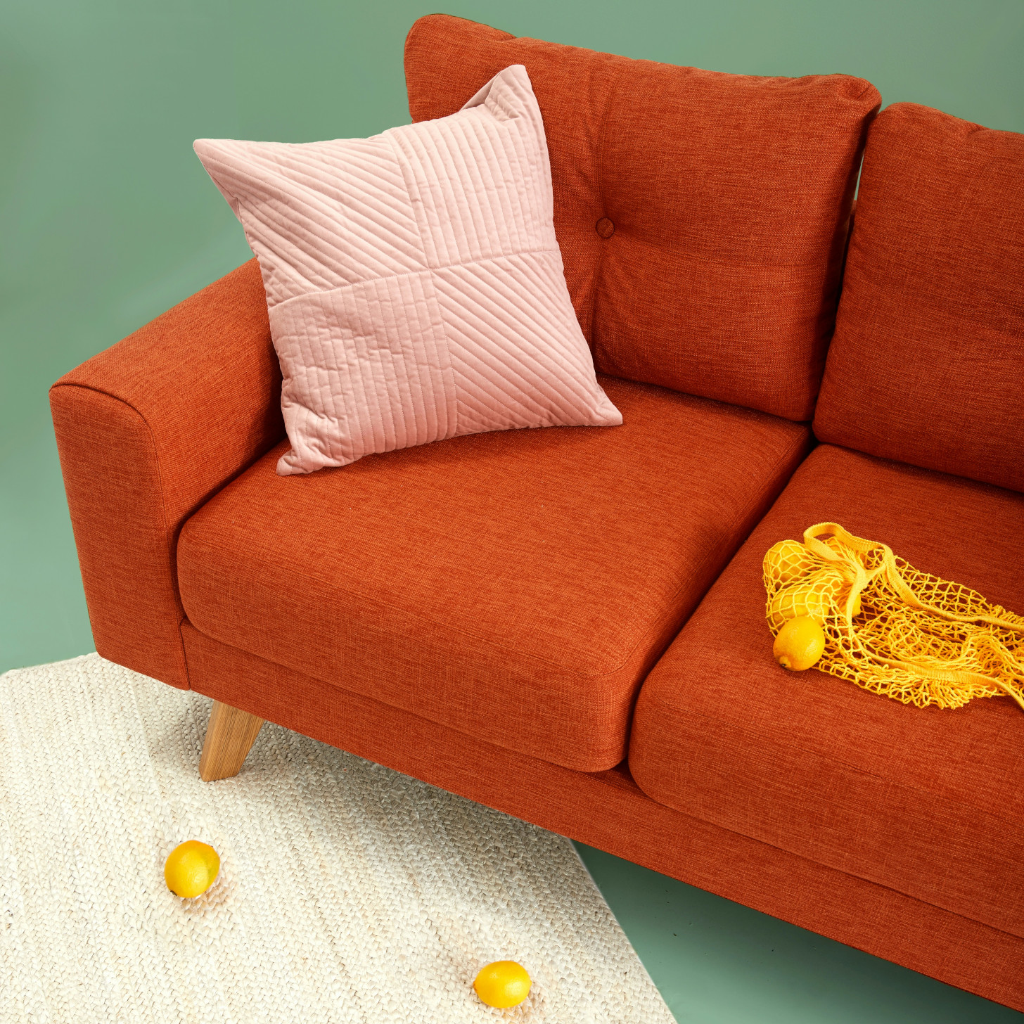 Beispiel für ein Basisbild: Ein rotes Sofa mit einem Sack Zitronen rechts und einem Zierkissen in der linken Ecke. Das Sofa steht schräg und ein Fuß steht auf einem weißen Teppich. Vor dem Sofa auf dem Teppich liegen zwei Zitronen.